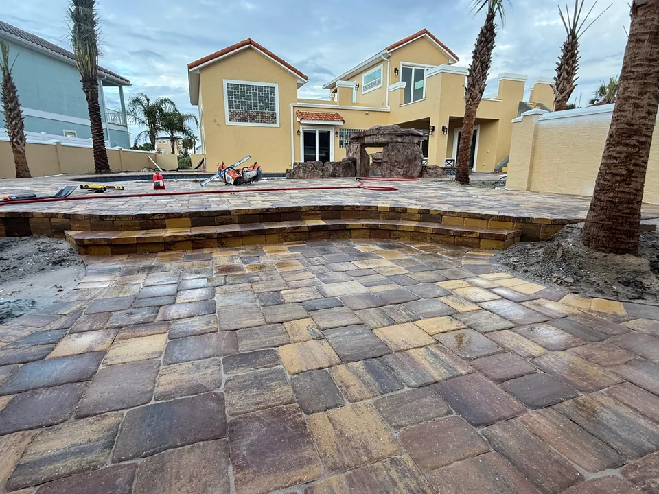 Multi-level paver patio under construction, with a raised pool terrace, paver-faced step risers and a wet saw on site
