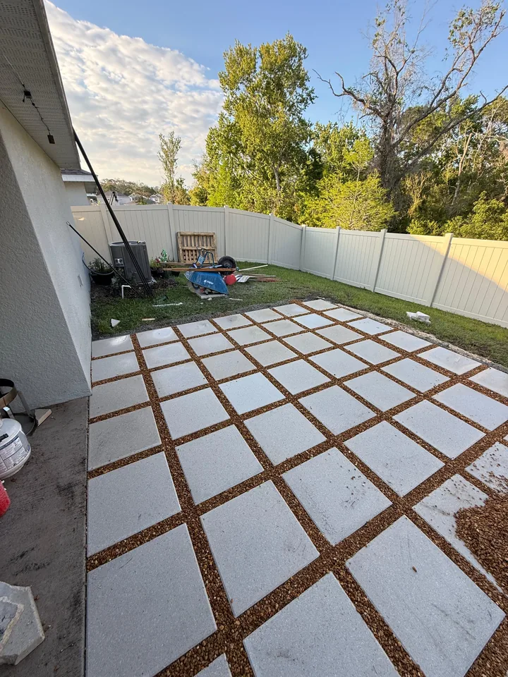 Backyard patio of large square concrete pavers laid on a compacted base with open gravel joints, fenced yard behind